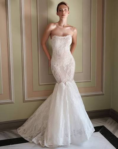 Elegant strapless lace wedding gown showcased on a model in a softly lit interior. The dress features intricate detailing and a mermaid silhouette.