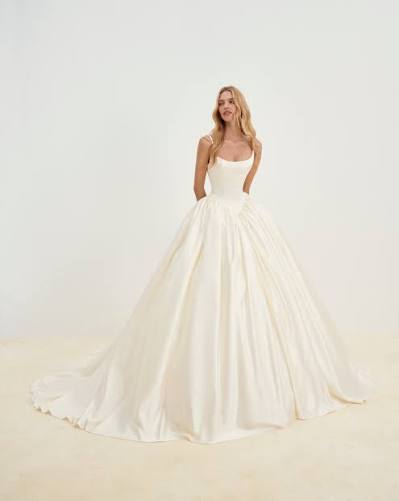 Elegant bride in a luxurious, flowing ivory ball gown, featuring a fitted bodice and a full skirt, posing against a neutral background.