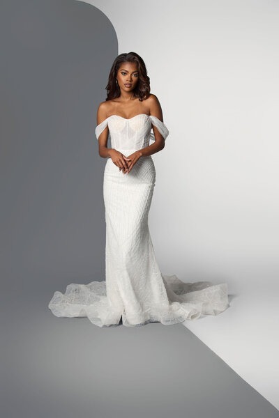 Elegant model in an off-the-shoulder white gown with a fitted silhouette and detailed train, showcasing bridal fashion. Perfect for wedding inspiration.