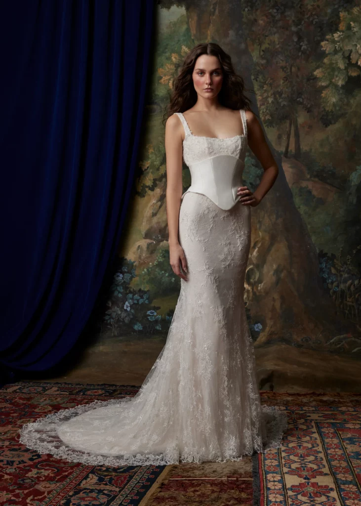 Model wearing an elegant lace wedding dress with a fitted bodice and flowing train, set against a vintage floral backdrop.