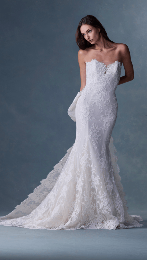 Elegant strapless wedding gown with detailed lace and a flowing train, showcased against a soft blue backdrop. Ideal for bridal fashion inspiration.