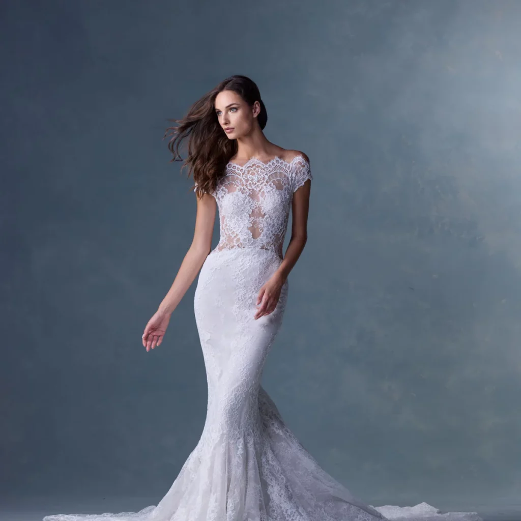 Elegant model in a sleek lace wedding gown with intricate detailing, posing against a softly blurred blue background. Ideal for bridal fashion inspiration.