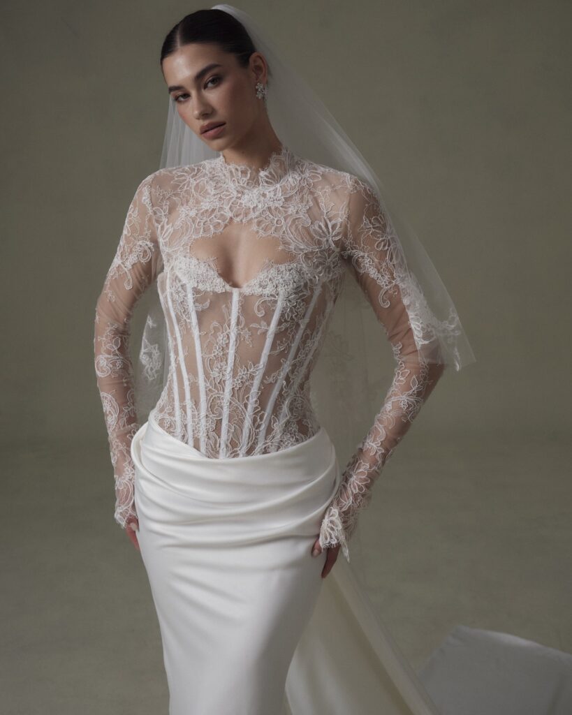 Bride in an intricate lace wedding gown with a fitted bodice and flowing satin skirt, complemented by a long veil. Elegant and sophisticated.